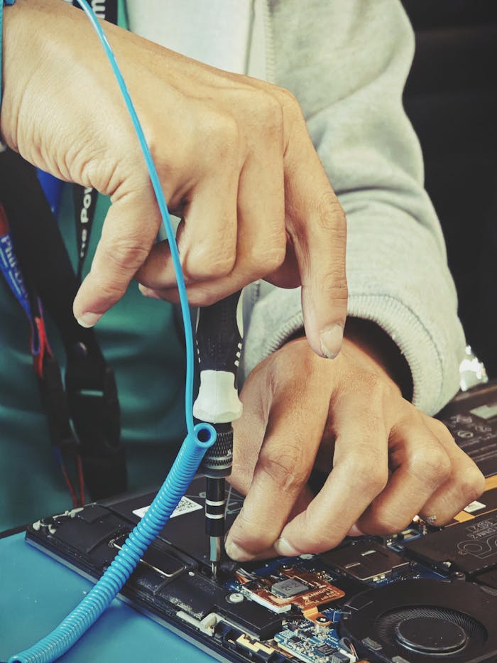 Close-up of a technicians hands repairing a laptops internal components with tools.